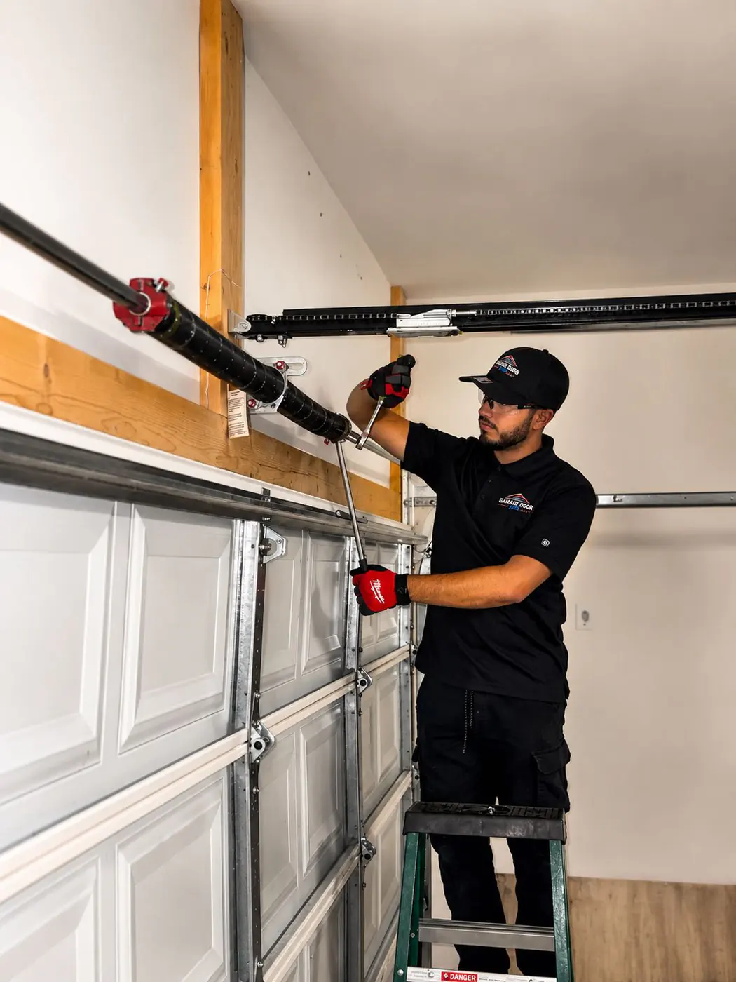 Technician on a ladder adjusting garage door hardware